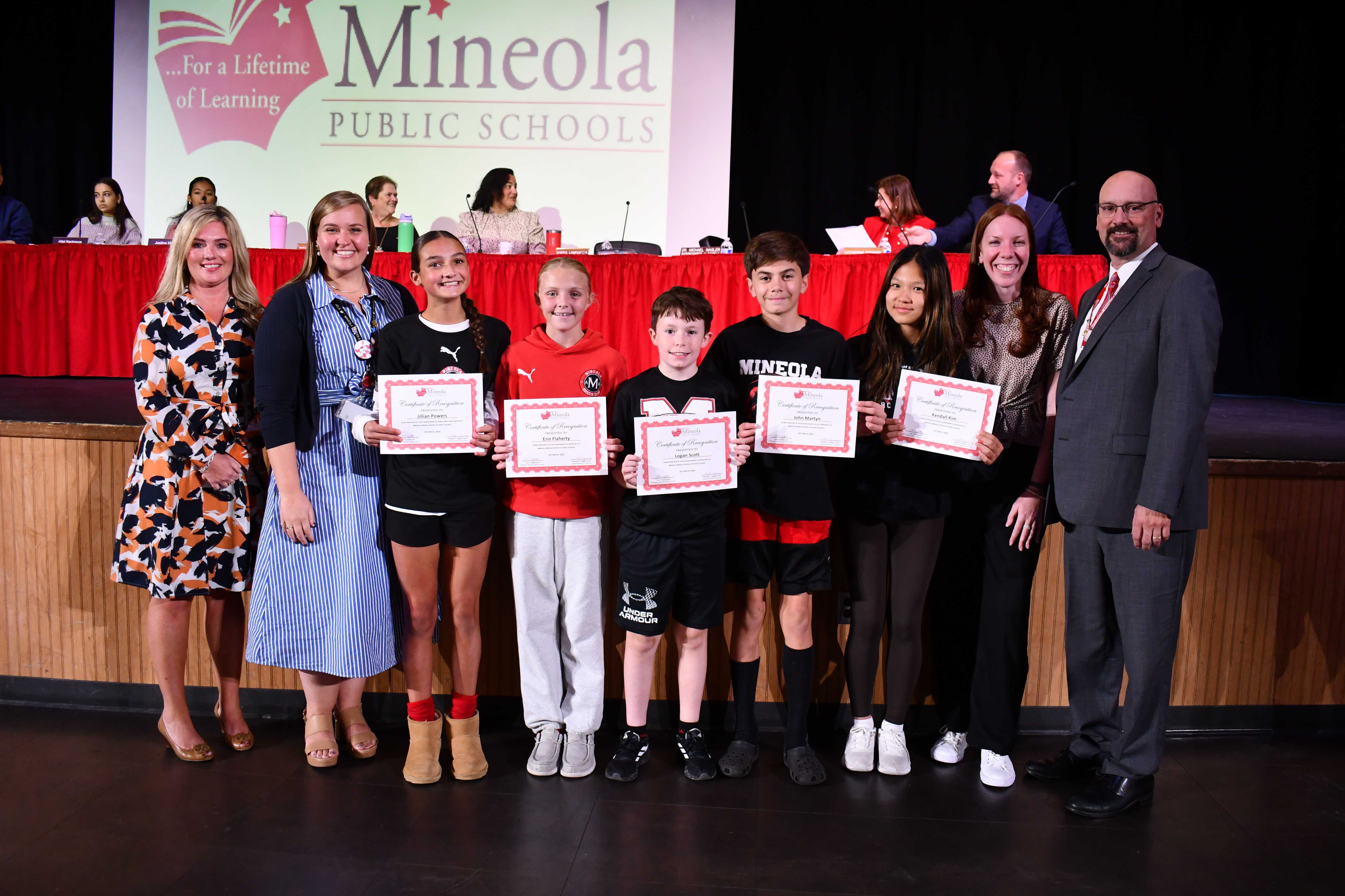 Students holding certificates for a photo with administrators at a board of education meeting